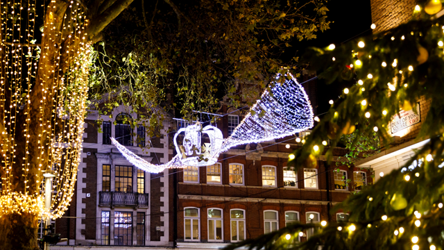 Christmas decorations hanging above the King's Road at night, including a bright LED crown and twinkling gold string lights with the side of a Christmas tree in the foreground