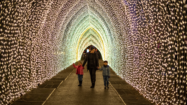 Une jeune femme tient la main à deux jeunes enfants et marche le long d'un tunnel illuminé à Kew Gardens.