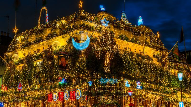 Snap photos of the breathtaking Christmas display that covers the front of Churchill Arms each year. Credit: Shutterstock. Image courtesy of Shutterstock. A photo of the Churchill Arms pub at Christmas covered in twinkling lights, trees and festive installations including a moon and