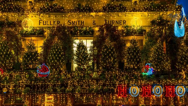 A photo of the Churchill Arms pub at Christmas covered in twinkling lights, trees and festive installations including a moon and "ho ho ho" lights 