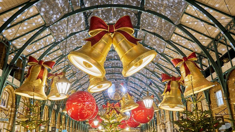 Giant gold bells with red bows and giant red baubles hang along the ceiling inside Covent Garden's covered market