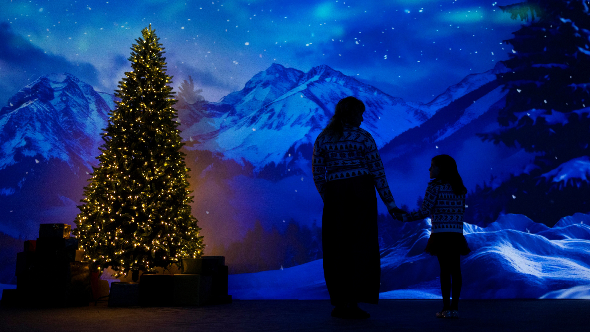 A photo inside Frameless gallery with a Christmas tree and snowy mountains on screen along with an outline of a mother and young child 
