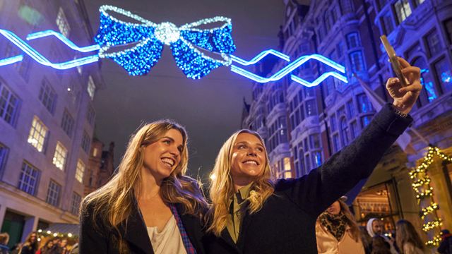 Deux jeunes femmes prennent un selfie dans le quartier de Mayfair illuminés de noeufs papillon bleus.