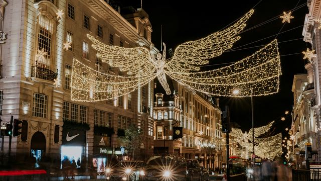 A photo of the Christmas lights hanging above Regent Street featuring warm twinkling lights in the shape of angels with giant wings with taxis, cars and people on the street below