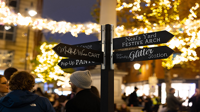 Un paneau de direction avec différentes activités de Noël se trouve dans le quartier de Seven Dials sous des illuminations festives.
