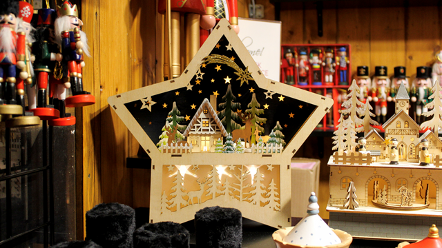 A wooden star decoration with a snowy festive scene inside hanging inside one of the Christmas market stalls in Kingston surrounded by toy shoulders