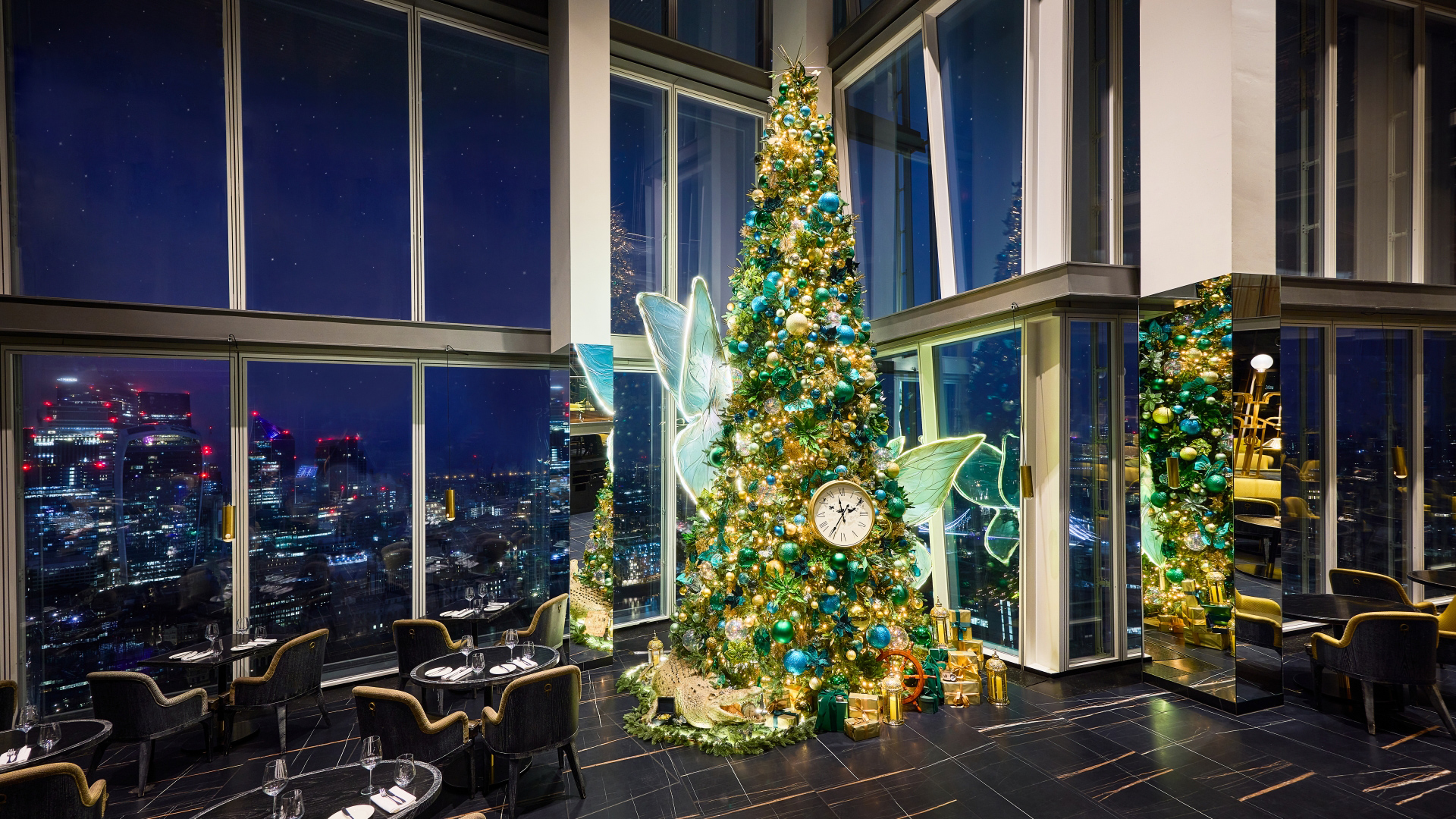 A photo of the Christmas tree in the corner of Aqua Shard with fairy wings and colourful lights and baubles in green hues with a clock decoration in reference to Peter Pan