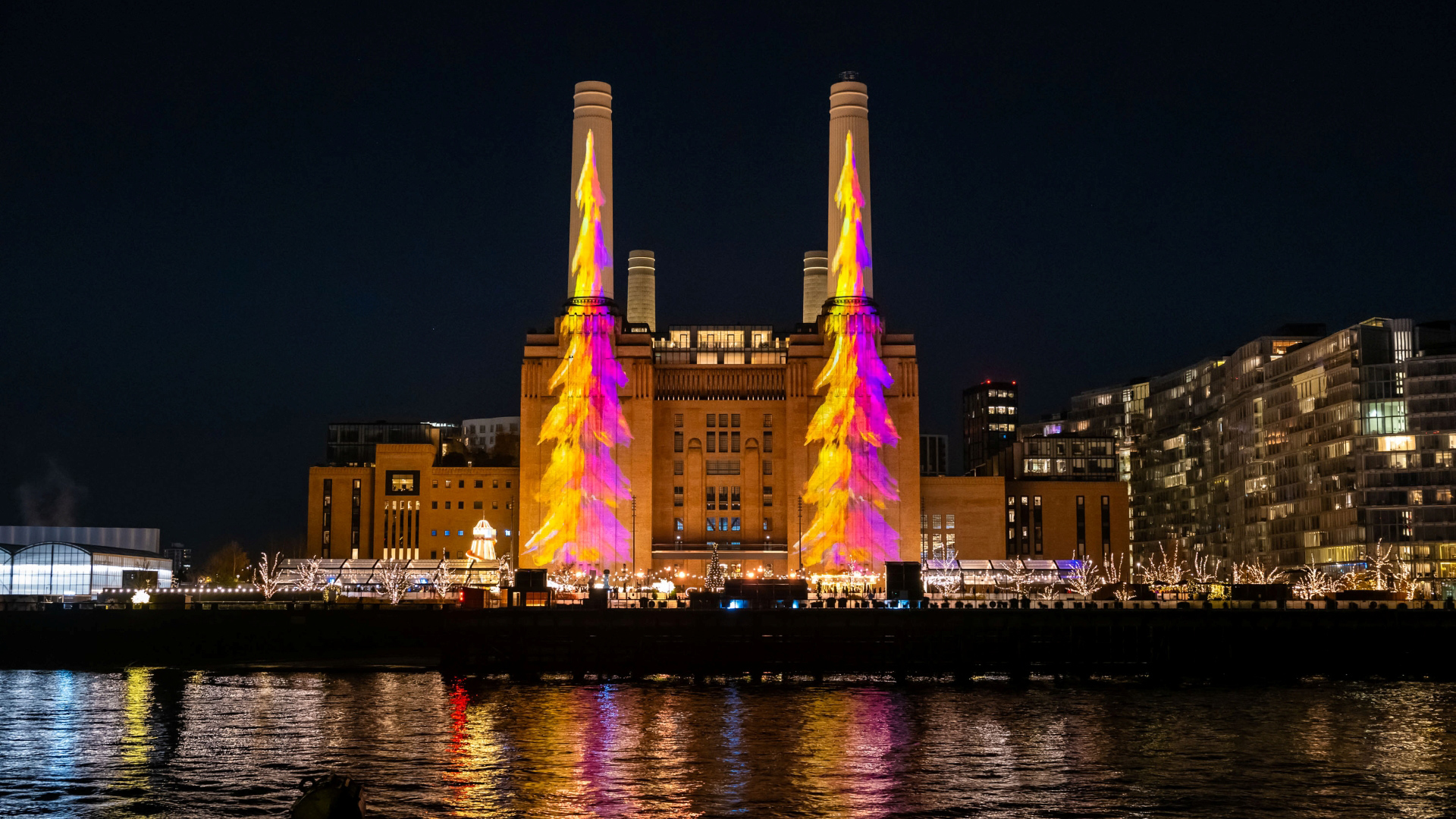 Battersea Power Station at night with a projection of two drawings of tall green Christmas trees with stars on top on both of its chimneys 