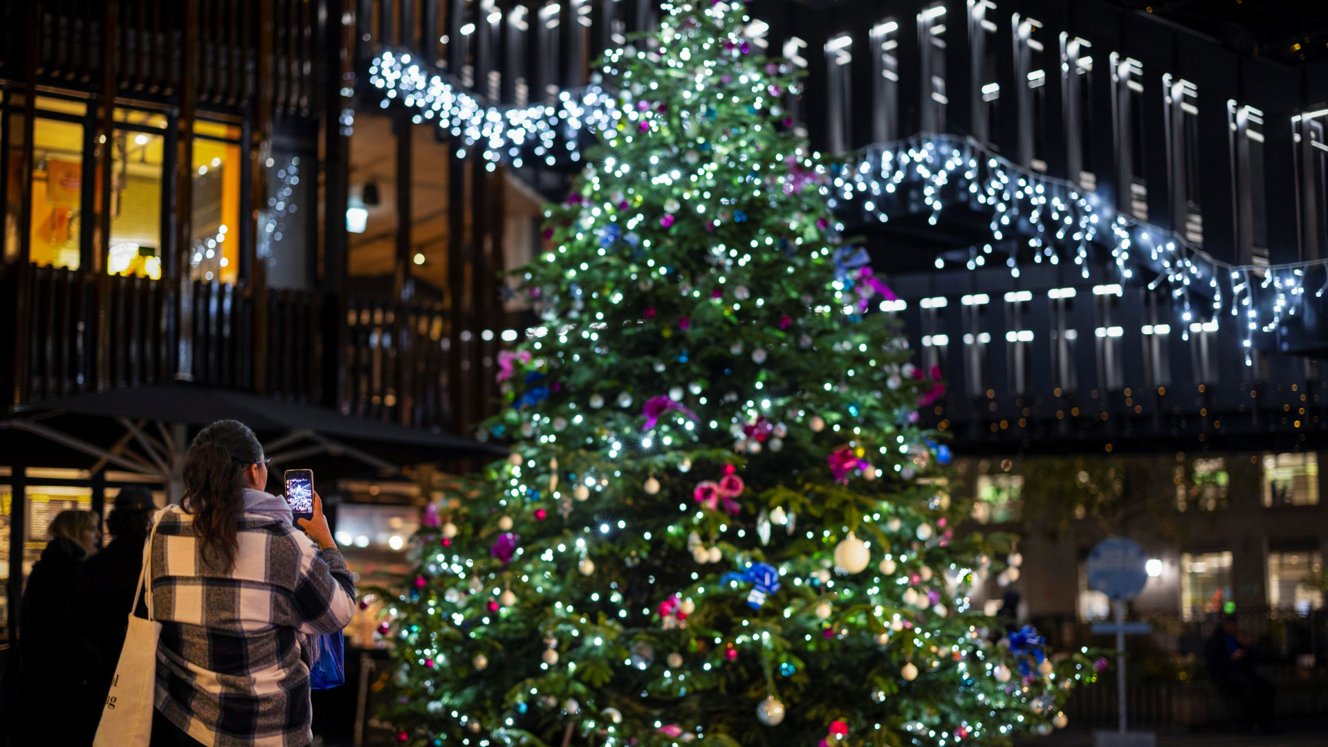 A large Christmas tree covered in twinkling lights and baubles stands outside of the Cyberdog shop in Camden Market, next to two giant silver robots wearing santa hats stood outside the shop entrance