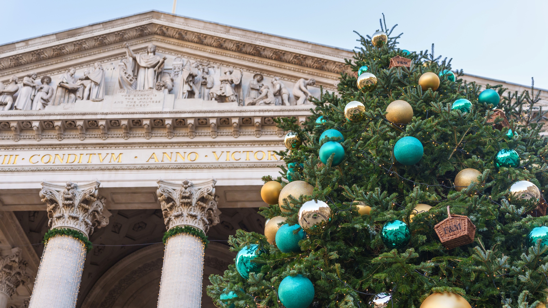 A photo of the Christmas tree in front of the Royal Exchange with blue and gold Fortnum and Mason baubles and twinkling lights around the building's columns