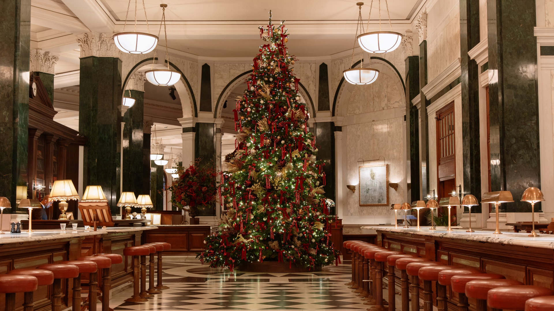A photo of a Christmas tree in the grand banking hall at The Ned decorated with red velvet bows and copper baubles