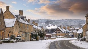 A traditional English village with country houses, winding roads and countryside covered in a dusting of light snow