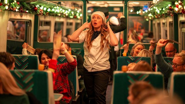 A performer dressed as a chef entertains passengers inside a festively decorated train carriage during THE POLAR EXPRESS™ Train Ride. Image courtesy of Pennington PR.