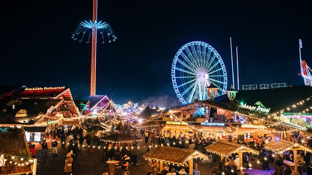 Twinkling string lights hang above people perusing wooden Christmas market stalls.