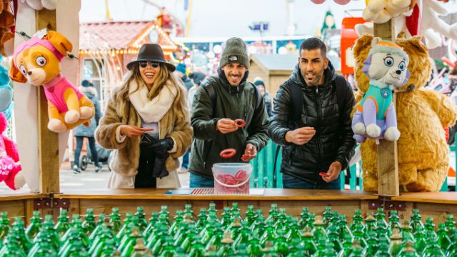 Genießen die die Spielmöglichkeiten im Winter Wonderland. Bild mit Genehmigung von C. Faruolo/Winter Wonderland. Drei Personen versuchen im Winter Wonderland London ein Ringwerfspiel zu gewinnen.