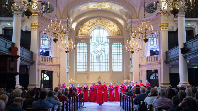 Choir wearing red coats singing, in the gold-coloured surroundings of St Martin's in the Fields.