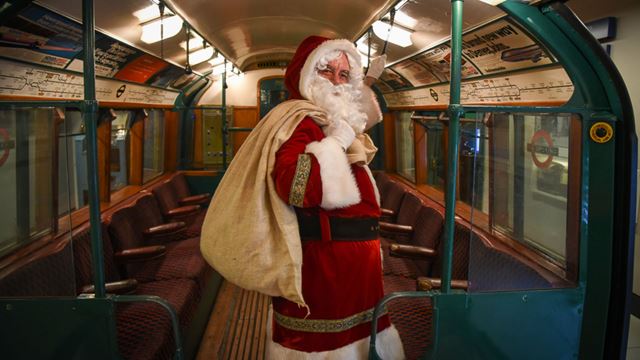 A man dressed in a Santa outfit holding a sack, in a London Tube. 