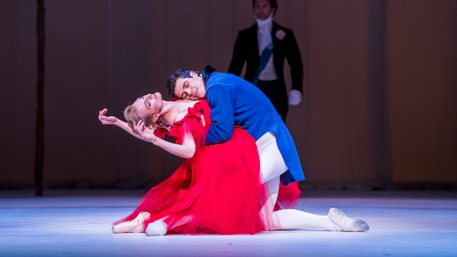 A man and a woman dancing on stage as part of Marguerite and Armand, wearing blue and red clothing.