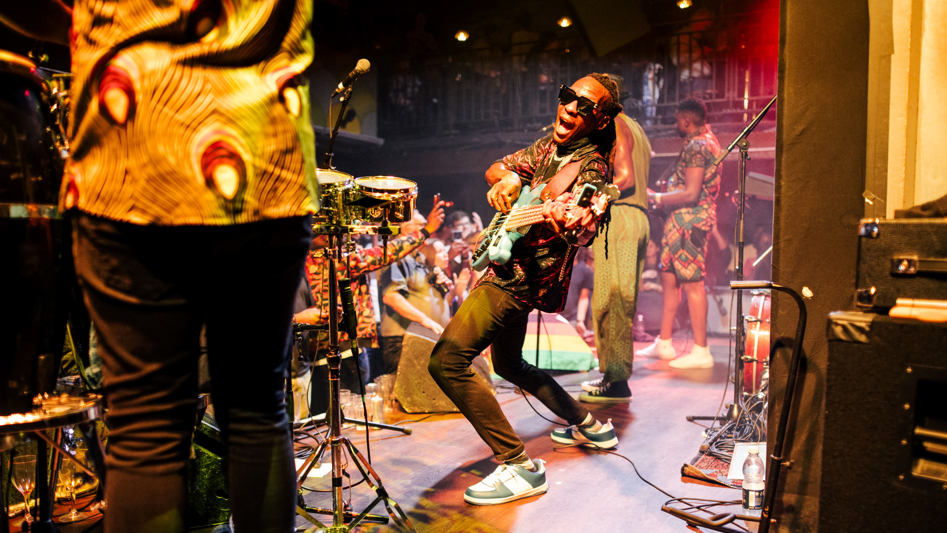 Guitarist looks into camera next to rest of band with crowd in the background