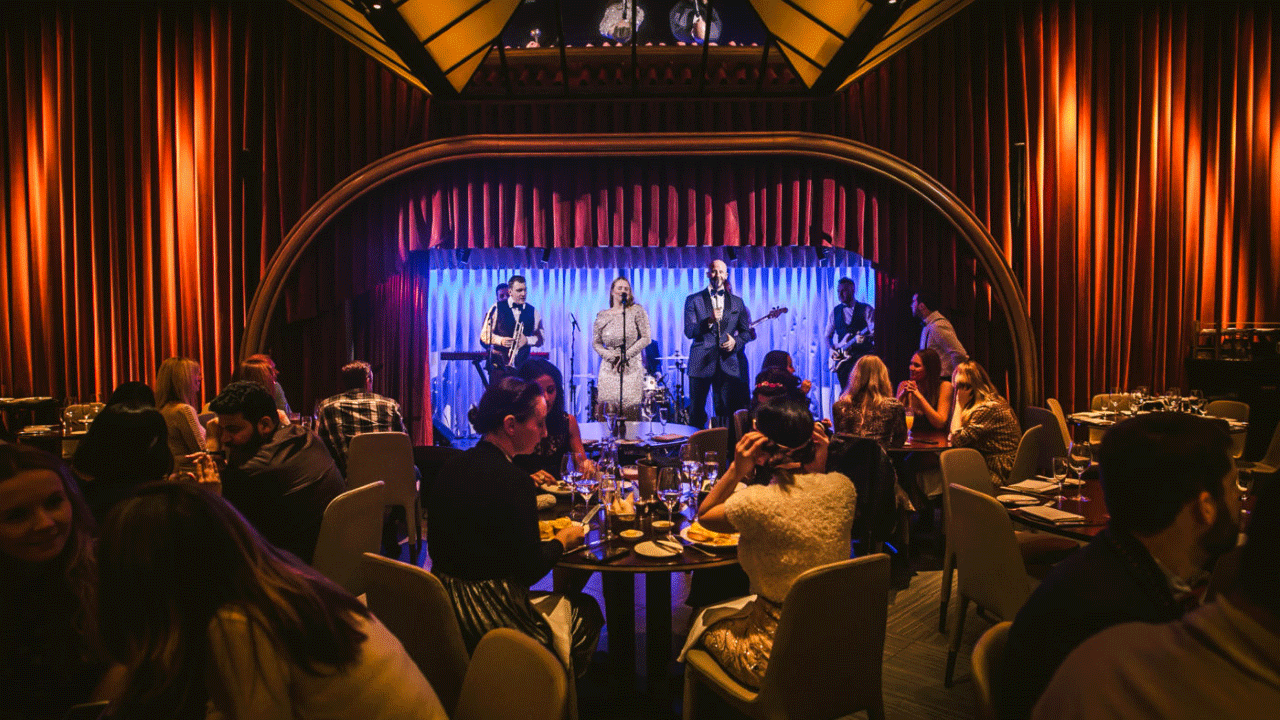 Band are illuminated with blue lights in front of tables of crowds