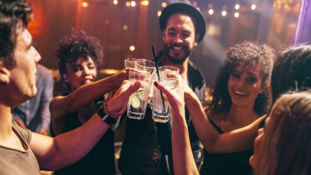 A group of people stand together dressed in party outfits and cheers their drinks on new years eve in london. 