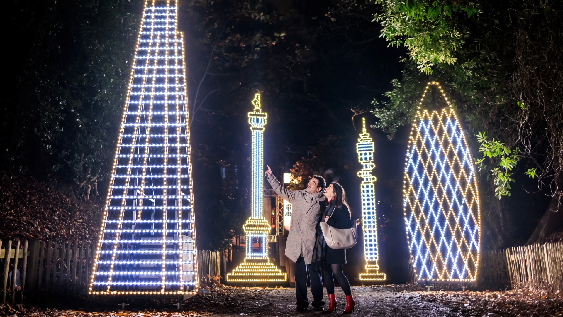 A photo of a man and woman pointing and looking up at a giant light installation of The Shard with other buildings in the background of London landmark inspired lights