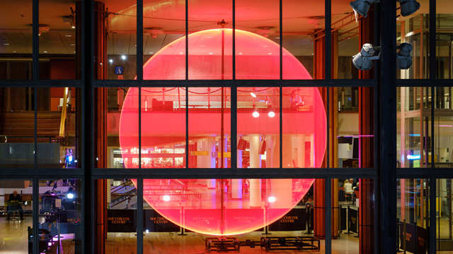 Une lumière rougeoyante géante projetée sur les fenêtres du Southbank Centre la nuit, avec l'entrée du bâtiment en contrebas.