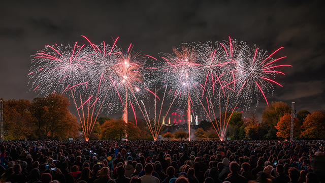 Battersea Park Feuerwerk. Bild mit Genehmigung von Enable Leisure and Culture. Rotes und weißes Feuerwerk, das während der Nacht über einer großen Menschenmenge mit der Battersea Power Station im Hintergrund explodiert.