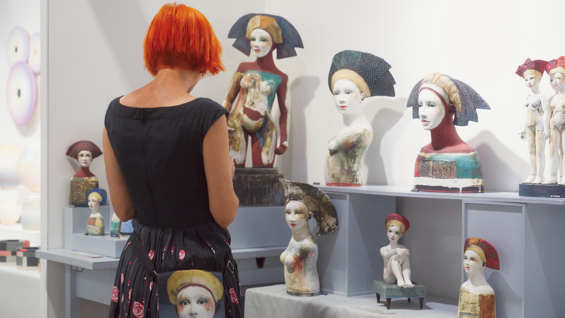 A person with red hair looks at decorative ceramic busts and sculptures.