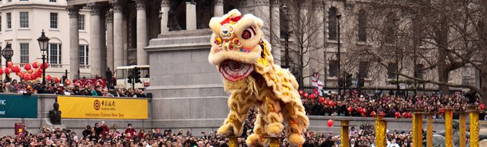 People, wearing a yellow lion dance costume, balance on yellow poles with a crowd of people behind in Trafalgar Square.