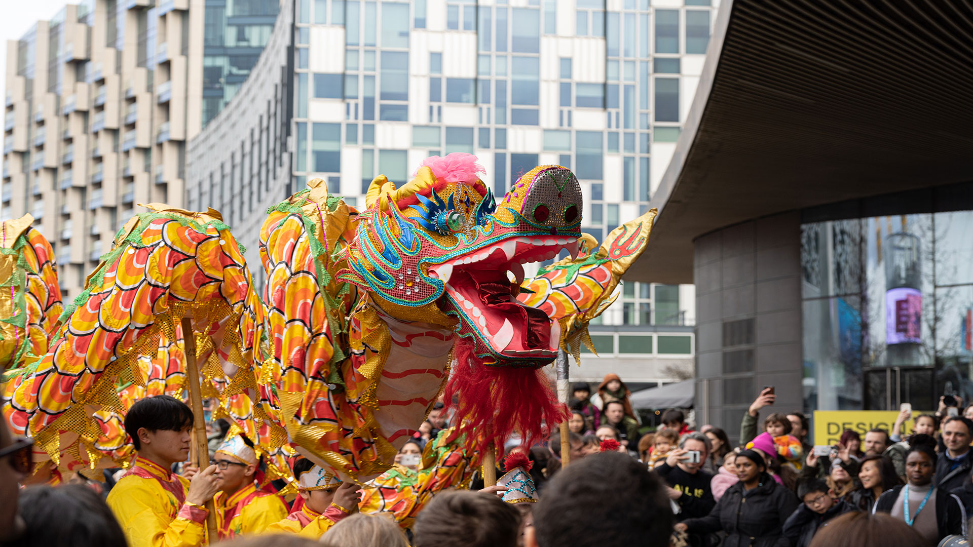 Celebrate Chinese New Year and watch some Dragon Dance at Greenwich Peninsula. Image Courtesy of LCA Dancers perform the Dragon Dance at Greenwich Peninsula surrounded by crowds of people and with big buildings in the background.