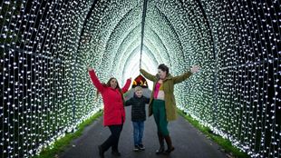 Une famille de trois personnes portant des manteaux d'hiver se tient sous le tunnel de lumière blanche à Noël à Kew.