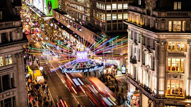 Rainbow-coloured Christmas lights sparkle above the buzzing streets of Oxford Street at night.