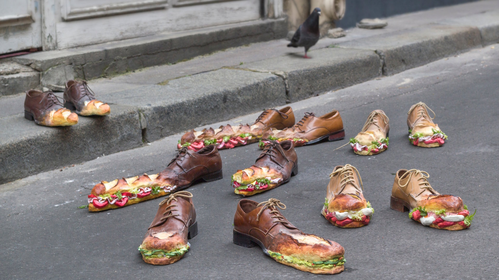  Jeanne Gourlaouen's The Sandwich Walk art installation on a road and pavement showing realistic brogue shoes featuring toe-caps that resemble baguette sandwiches.