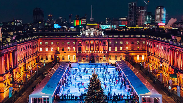 Une vue aérienne nocturne de la patinoire extérieure de Sommerset House avec une vue sur la ville de Londres en arrière plan.