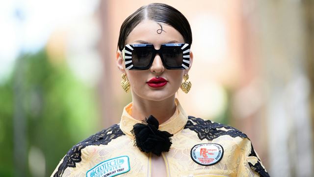 London Fashion Week model wearing large square sunglasses and a yellow jacket with colourful patches.
