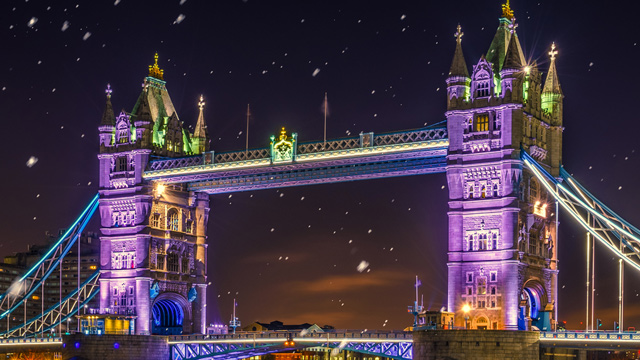 Tower Bridge est illuminé de nuit d'une couleur violette avec quelques flocons de neige tombant sur la Tamise.