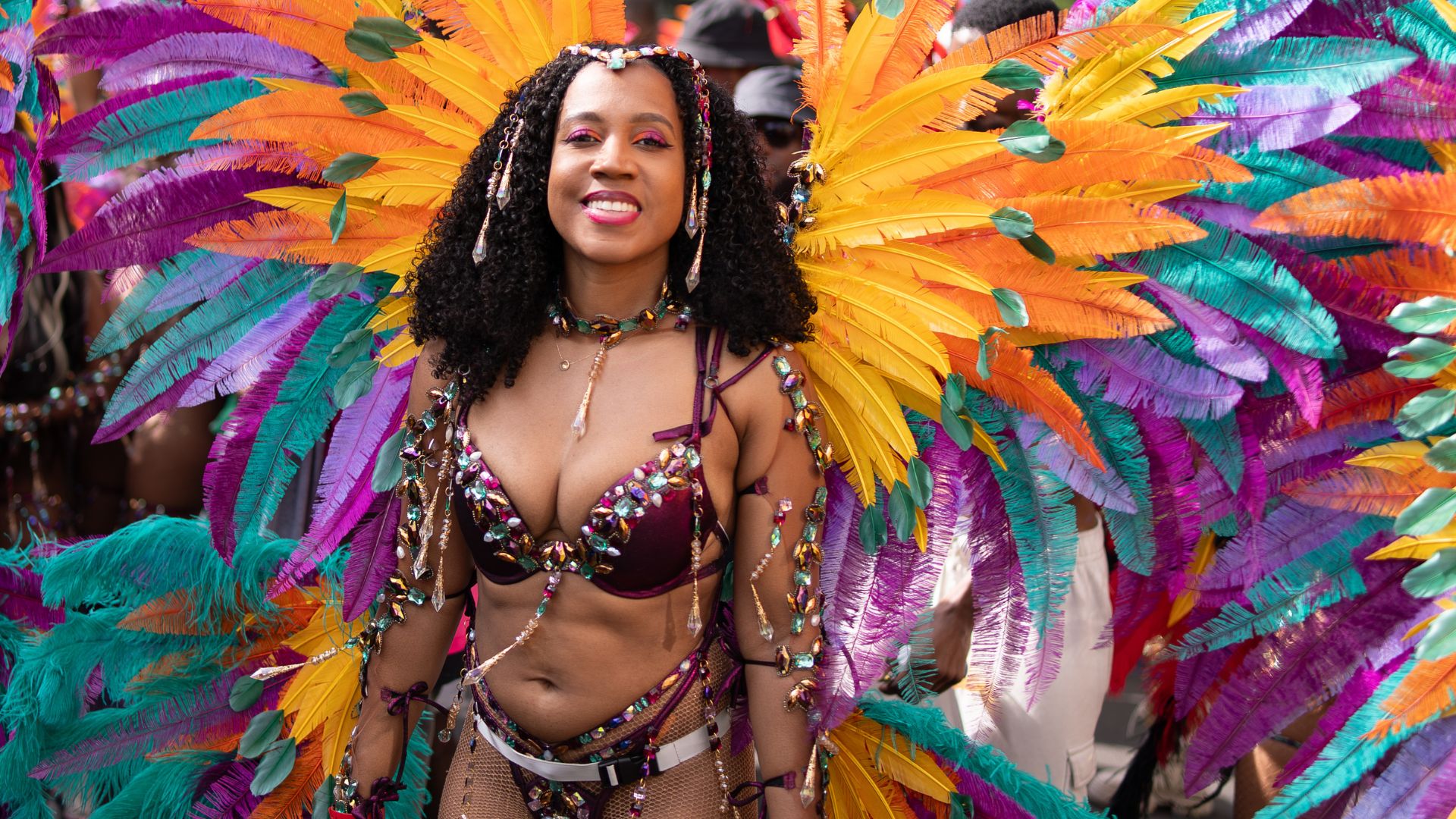 A carnival performer wears a vibrant costume with orange, yellow, purple and turquoise feathers at Notting Hill Carnival