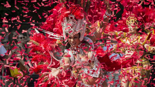 Un artiste du carnaval de Notting Hill danse entouré de confettis rouges.