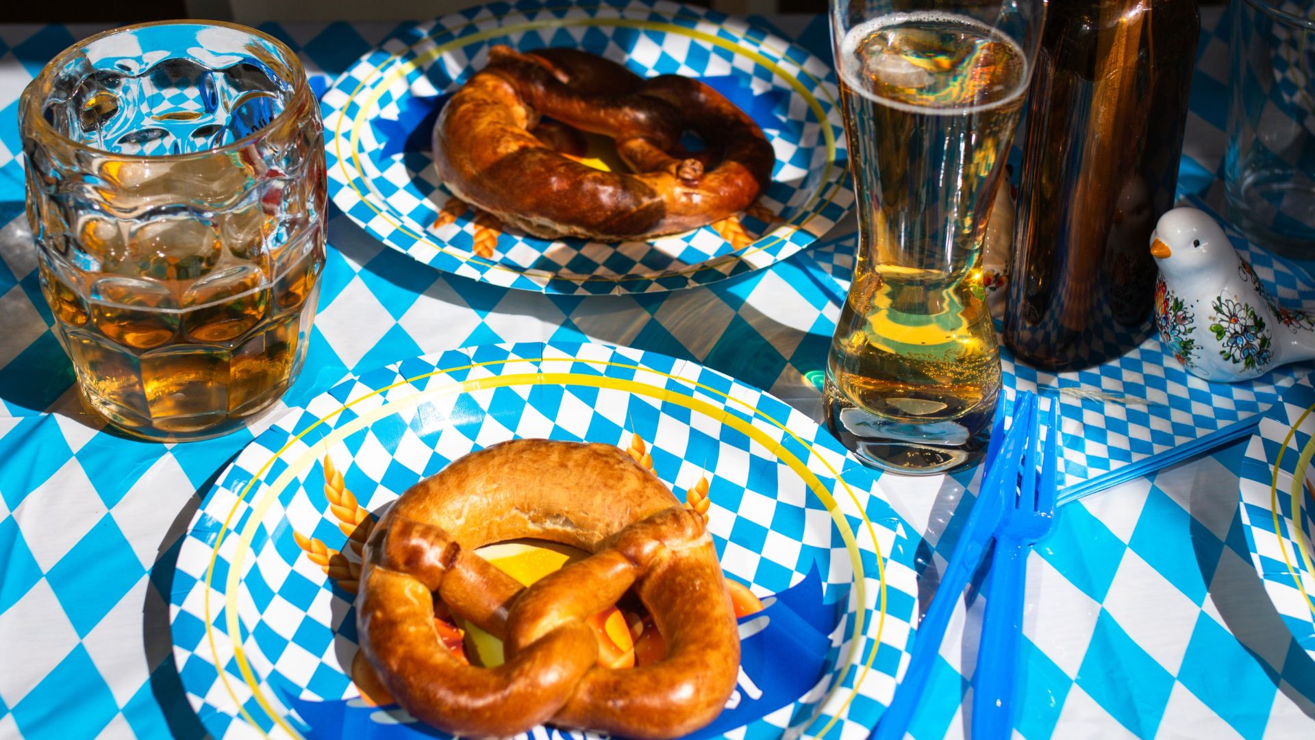 Table with blue and white checkered tablecloth, matching plates, traditional German pretzels and glasses of beer.