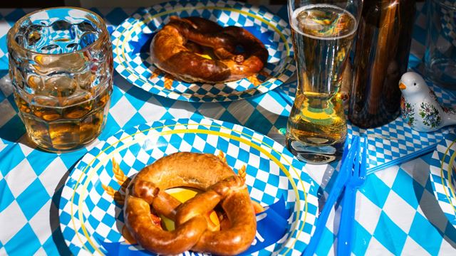 Table with blue and white checkered tablecloth, matching plates, traditional German pretzels and glasses of beer.