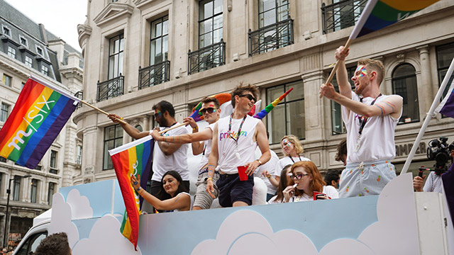 People standing up on a float, waving rainbow flags, as they travel along during the Pride in London parade.