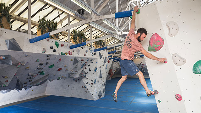 Wall to wall climbing at The Arch Climbing Wall Bermondsey © Andy Day /The Arch Climbing Wall. A man in a pink t-shirt and shorts climbing the wall at The Arch Climbing Wall in Bermondsey.