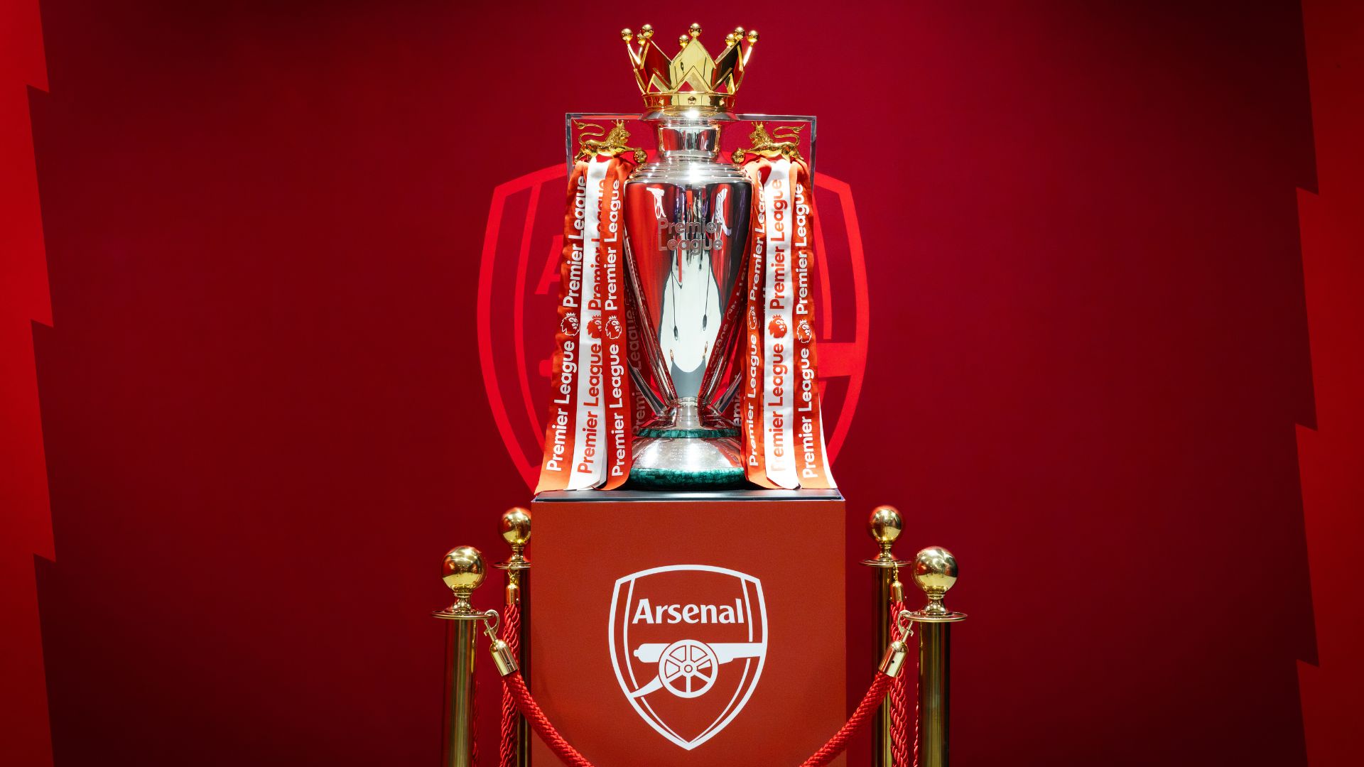 Silver Premier League trophy on a red Arsenal-branded podium against a red backdrop.