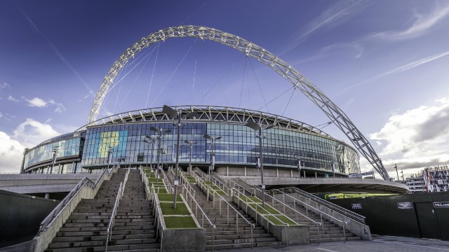 Wembley Stadium is England's national stadium. ©visitlondon.com/Antoine Buchet. The outside of Wembley Stadium viewed from the bottom of the entrance steps with the venue's iconic arch emphasised against the blue sky.