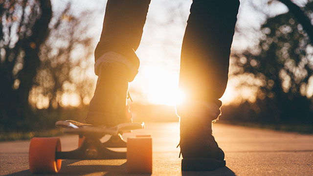 A skateboarder with one foot on the ground on a sunny evening