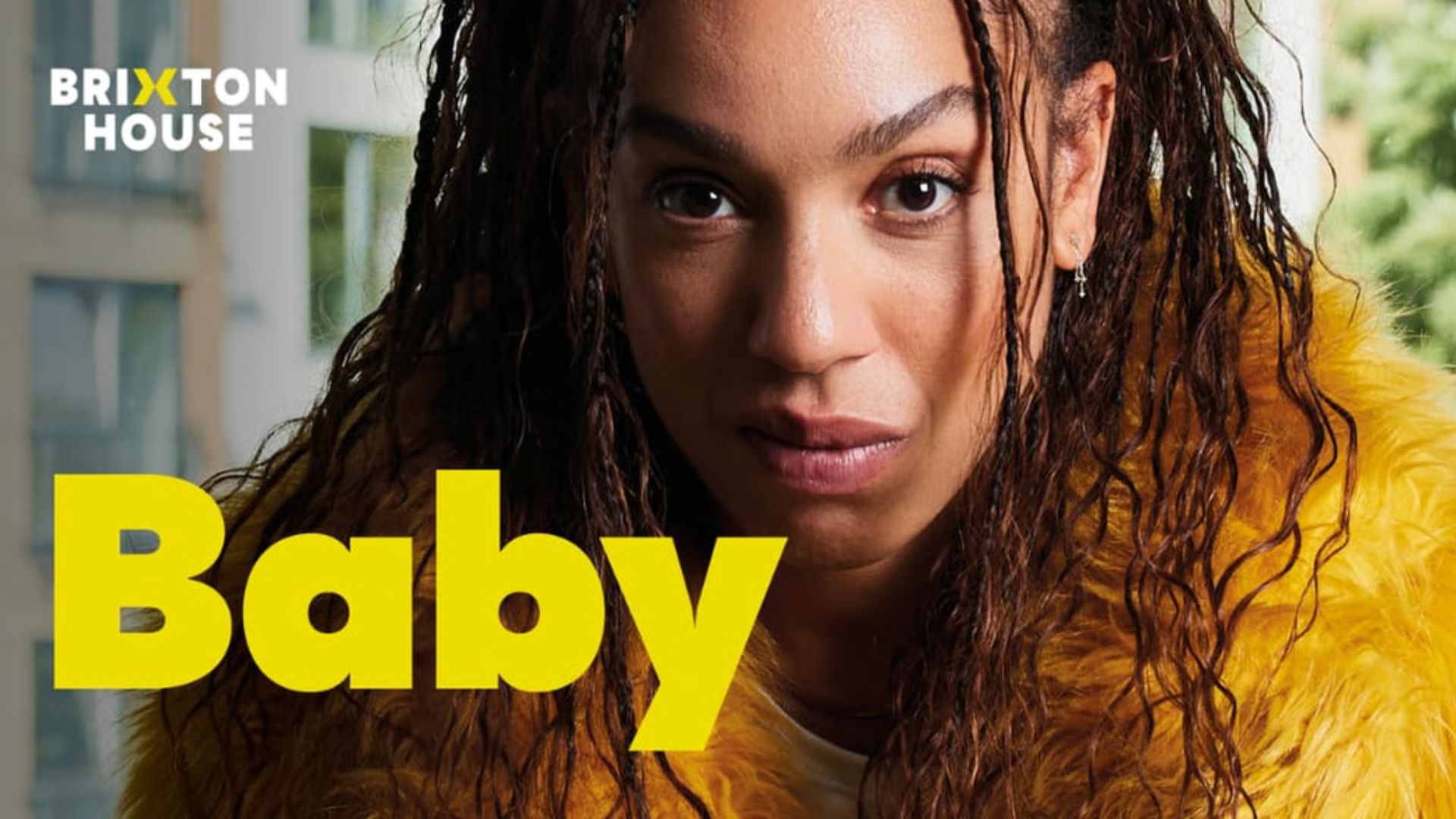 Pearl Mackie wearing a yellow fluffy coat with yellow graphics spelling out 'Baby'
