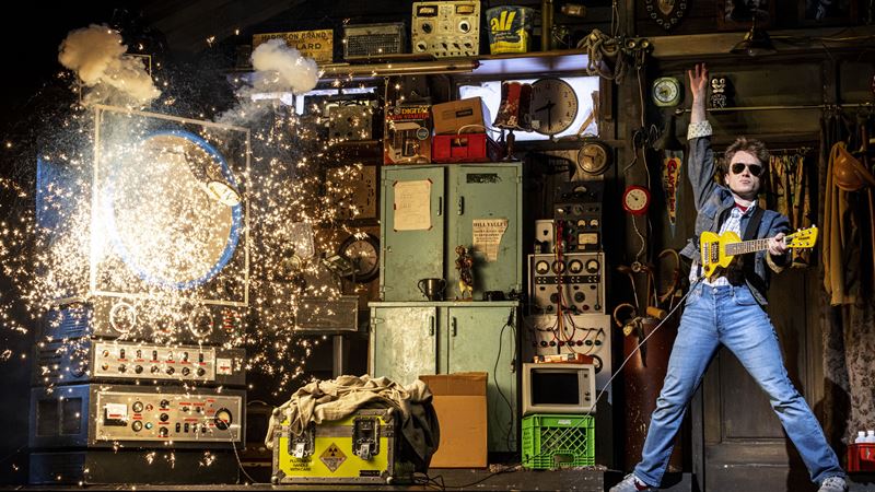 Marty McFly plays electric guitar while a machine explodes in the background.