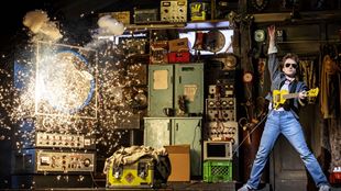 Marty McFly plays electric guitar while a machine explodes in the background.