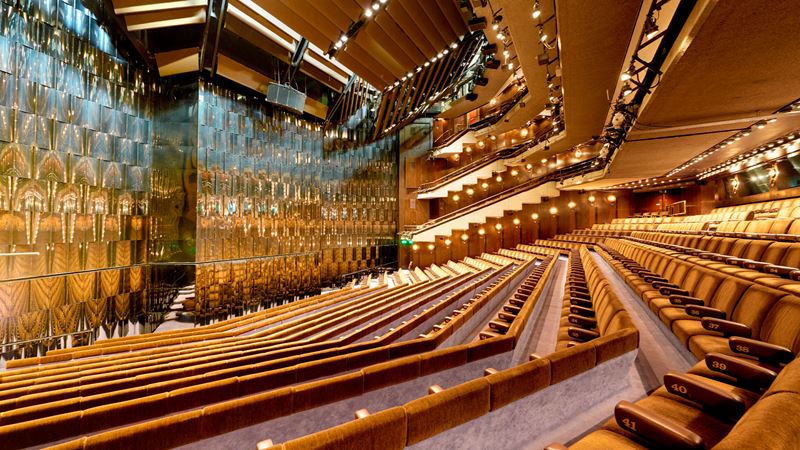 Head to the Barbican Theatre and experience one of its groundbreaking productions. Credit: Peter Dazeley. Image courtesy of the Barbican. The auditorium of the Barbican Theatre stands empty, with its ochre seats and silver, gleaming walls.